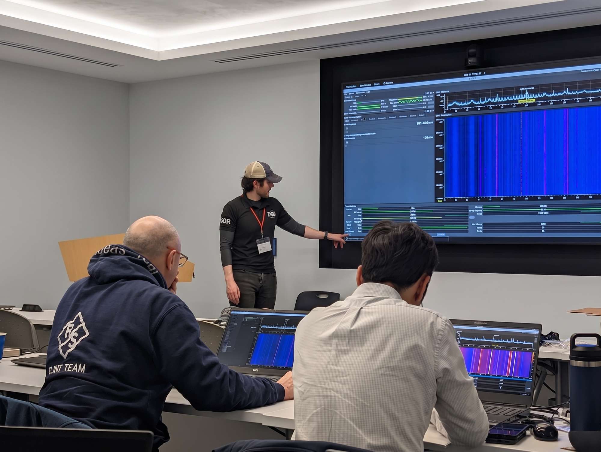 3dB Labs instructor pointing at a wall display running a live Sceptre waterfall while two operators follow along on their own Sceptre laptops