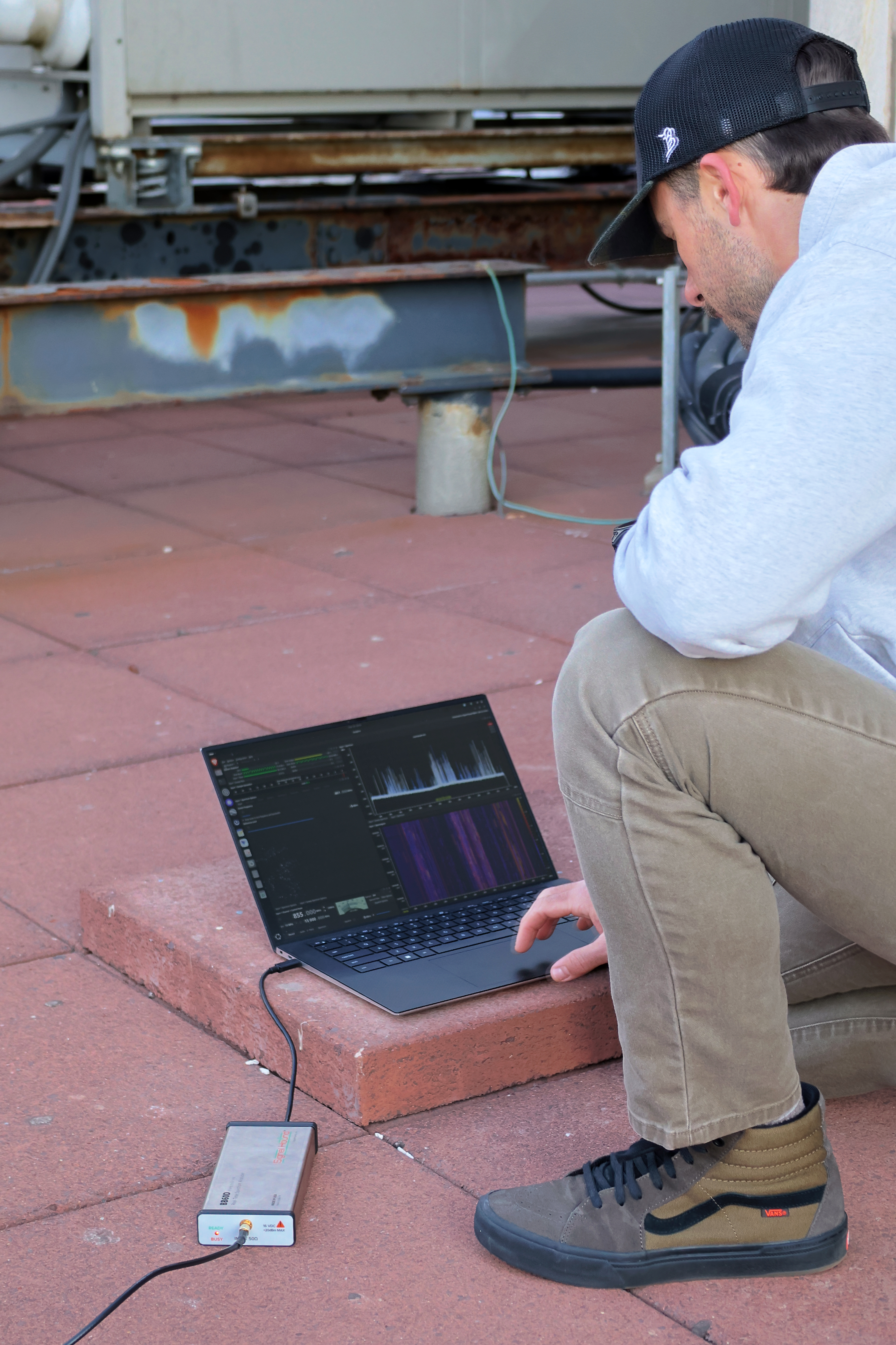 3dB Labs engineer on a rooftop running a Sceptre spectrum survey on a laptop tethered to an SDR